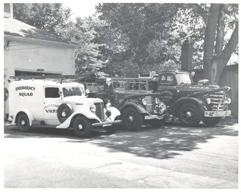 Three vintage Florissant Valley Volunteer Fire Department apparatus lined up outside an early firehouse