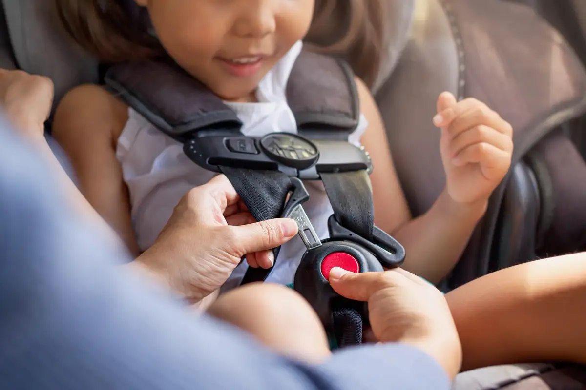A child being buckled into a properly installed car safety seat